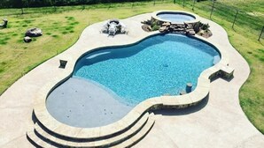 A swimming pool with a curved design, surrounded by a stone deck and a grassy area.