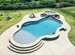 A swimming pool with a curved design, surrounded by a stone deck and a grassy area.