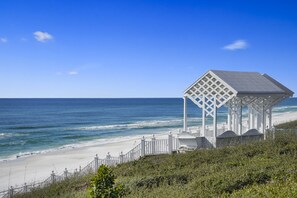 A beach gazebo with a lattice roof overlooking the ocean.