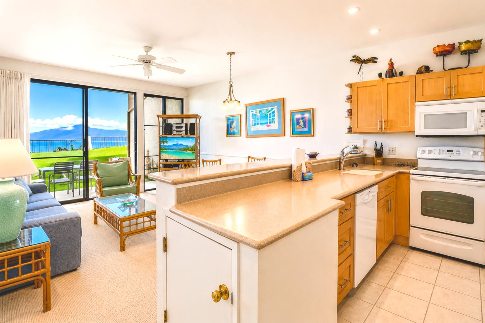 A modern kitchen with a large island, wooden cabinets, and a view of the sea through the sliding glass doors.