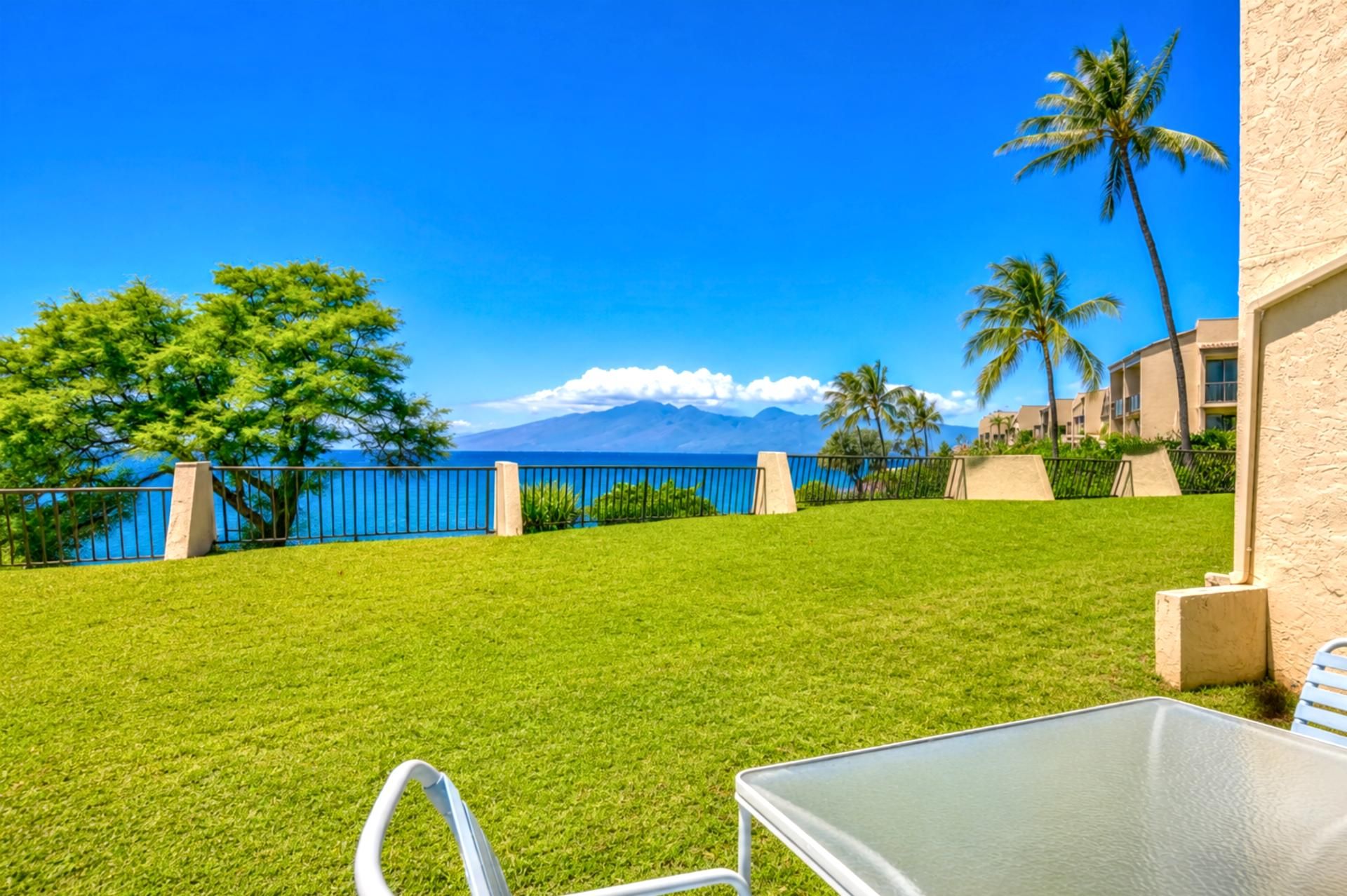 A grassy lawn with a view of the ocean and mountains, a metal table, and a chair.