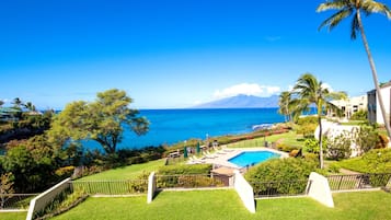 A pool area with a view of the ocean and a mountain in the distance.