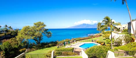 Zona de piscina con vista al océano y una montaña al fondo.