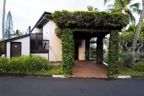 Una casa con entrada cubierta, un pequeño porche y un jardín con plantas tropicales.