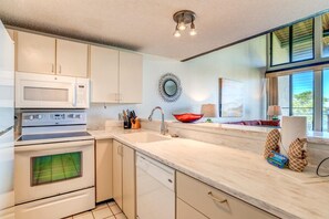 Una cocina moderna con armarios blancos, microondas, estufa y lavavajillas. Se ve una ventana con vista a zonas verdes.