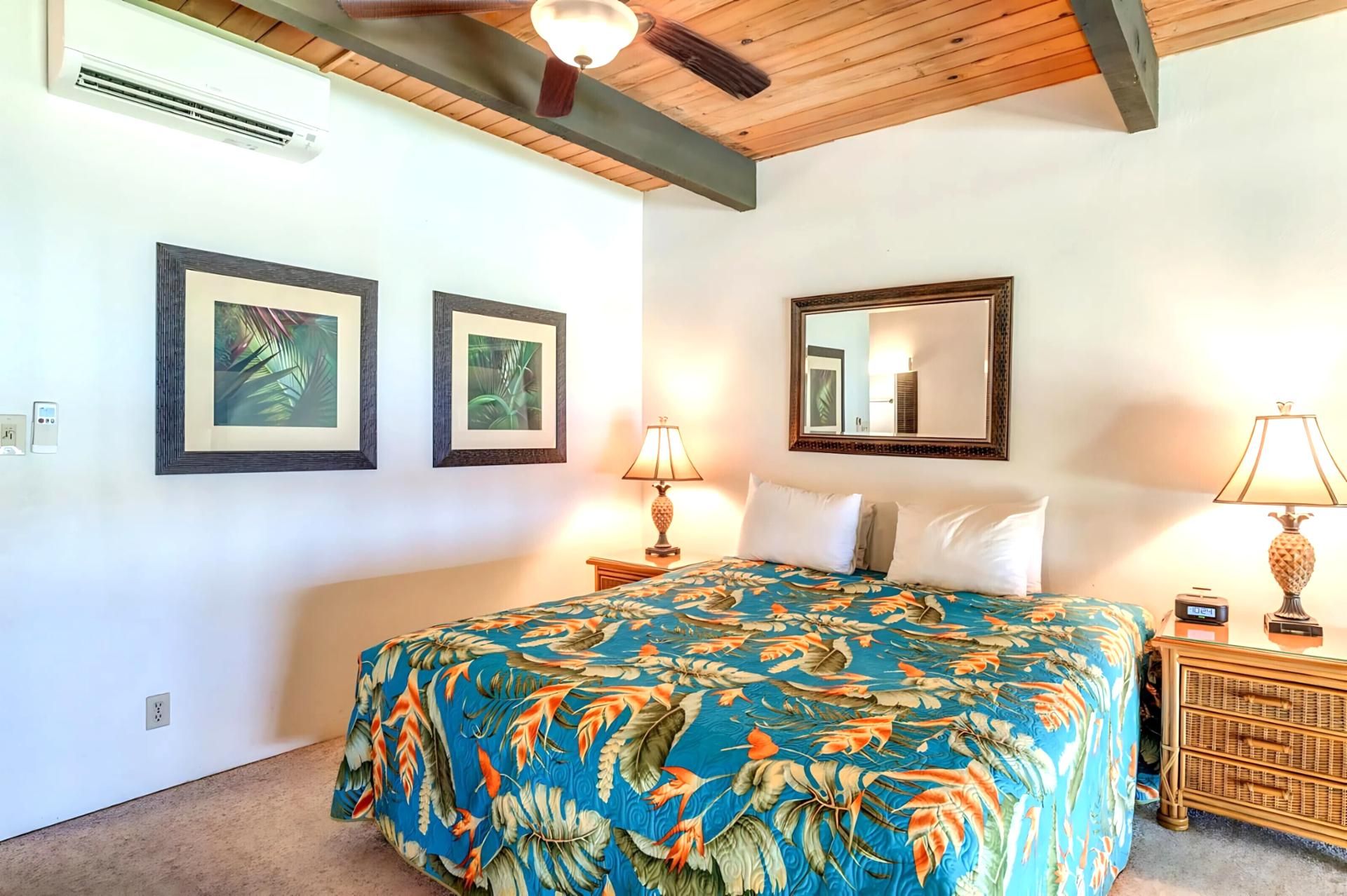 A bedroom with a bed, two wall-mounted picture frames, a ceiling fan, and a bedside table with a lamp.