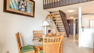 A dining area with a round glass table, wicker chairs, and a lamp. A staircase leads to an upper level.
