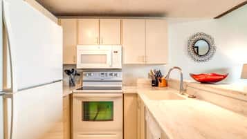 Cocina compacta con armarios blancos, microondas, horno y lavabo con un tazón rojo sobre la encimera.