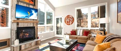 A living room with a fireplace, a large TV, and a sofa with cushions.