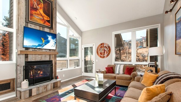 Una sala de estar con chimenea, televisor, sofá y un amplio ventanal.