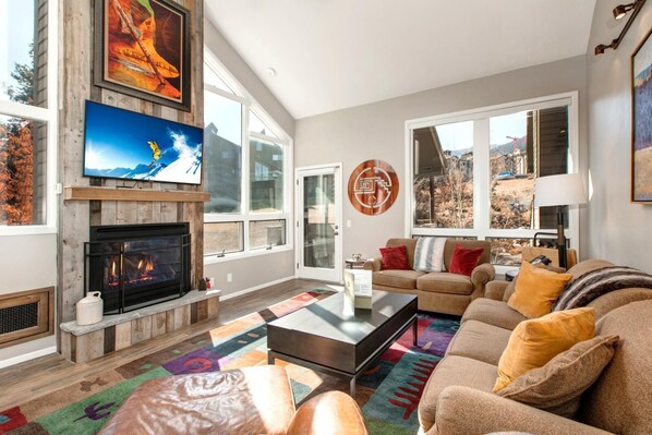 Una sala de estar con chimenea, televisor, sofá y un amplio ventanal.