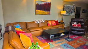 A living room with a sofa, armchair, coffee table, and a colorful rug.