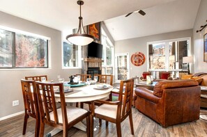 A dining area with a round table, wooden chairs, and a chandelier. There is a sofa and a fireplace in the background. - KBM Resorts | Red Pine | Free Door-to-Ski shuttle, Near Gondola at Canyons and Village,Common hot tub, Pool (summer), Tennis, Gas Fireplace RPT-14t (Park City)