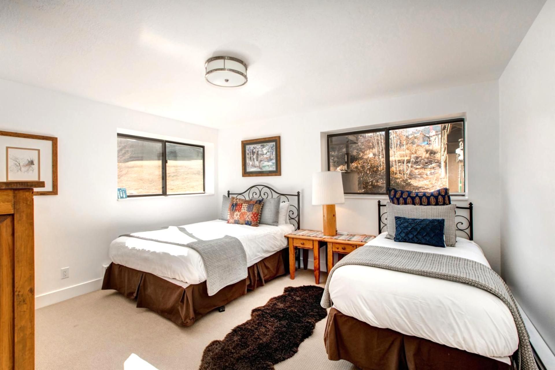 A bedroom with two beds, a wooden nightstand, a lamp, and a rug.