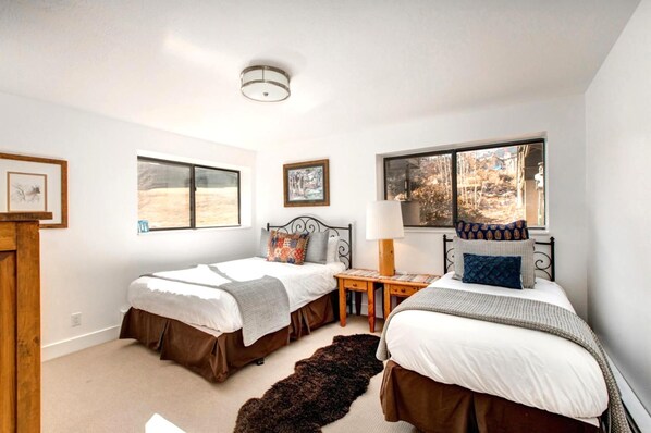 A bedroom with two beds, a wooden nightstand, a lamp, and a rug.