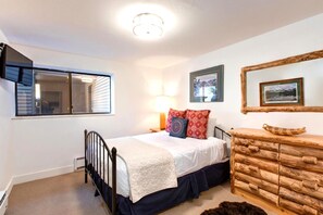 A bedroom with a bed, a wooden dresser, a mirror, and framed pictures on the wall.