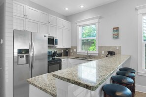 A modern kitchen with white cabinetry, stainless steel appliances, a granite countertop, and a window with a view of greenery.