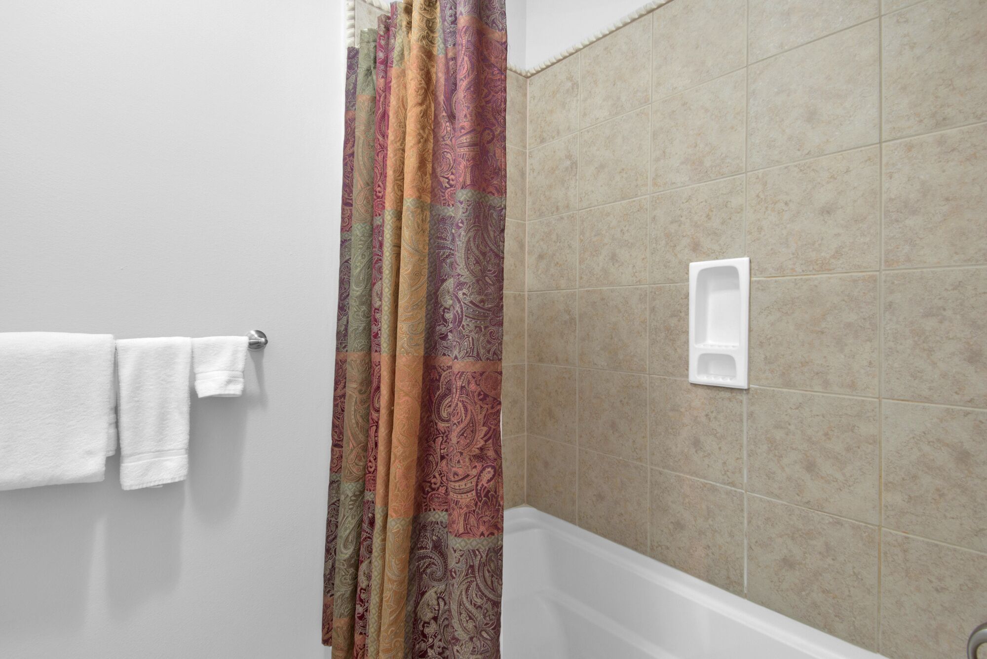 Une salle de bain avec un rideau de douche, un porte-serviettes avec des serviettes blanches et une baignoire blanche.