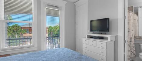 Un dormitorio con cama, televisor en una cómoda blanca y balcón con persianas.