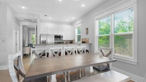 A modern kitchen with white cabinetry, a large island with seating, and a view of greenery through the windows. - Townhome-Comm Pool-Private Beach Access 5 Min Walk (Miramar Beach)
