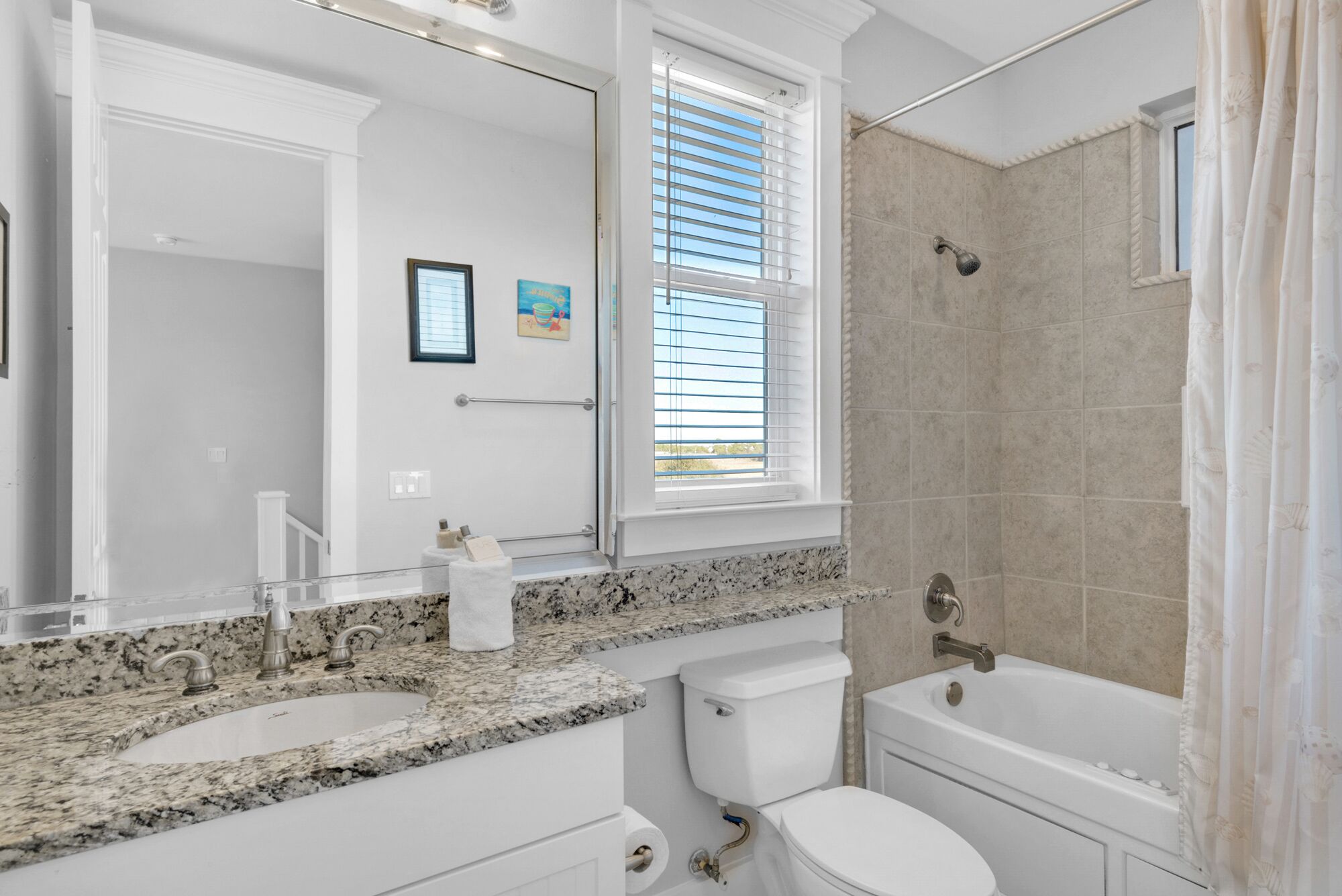 Un baño con lavamanos de encimera de granito, inodoro y bañera.