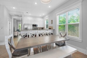 A modern kitchen with white cabinetry, a large island with seating, and a view of greenery through the windows.