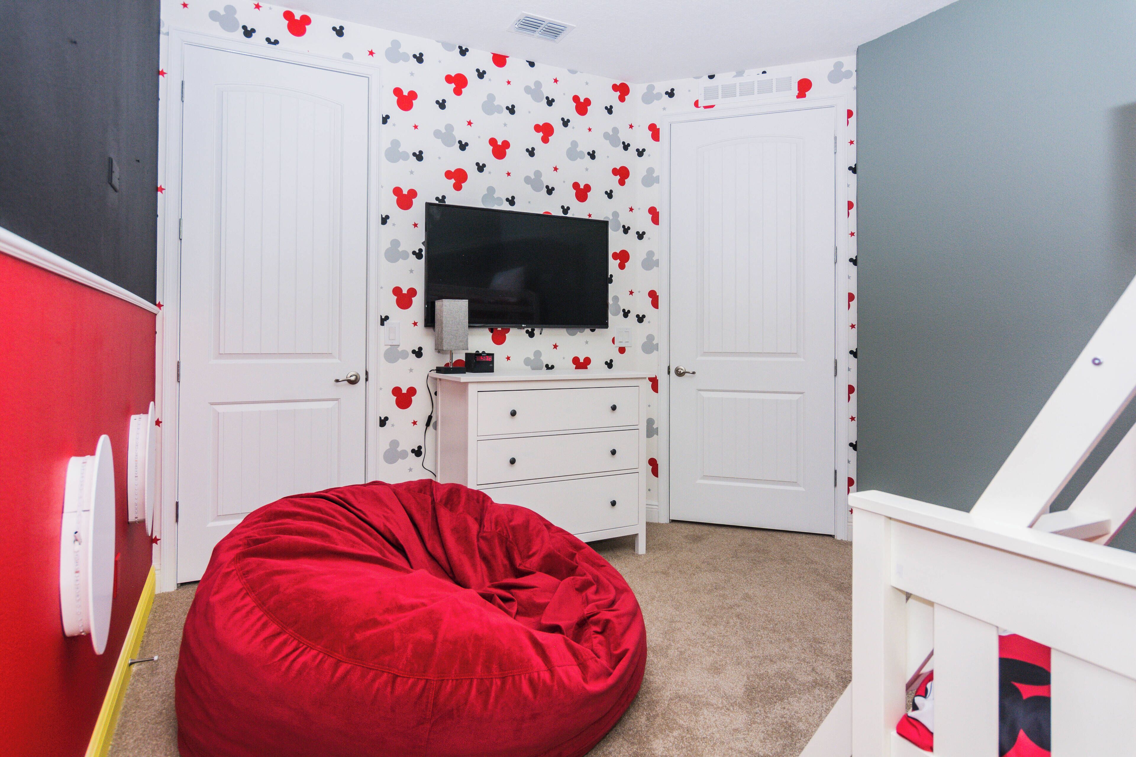 A room with a red bean bag chair, a TV mounted on a wall, and a white dresser.