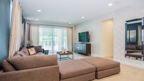 A modern living room with a sectional sofa, a TV mounted on the wall, and a large window with curtains. - Gorgeous Single Home With Private Pool at Encore (Kissimmee)