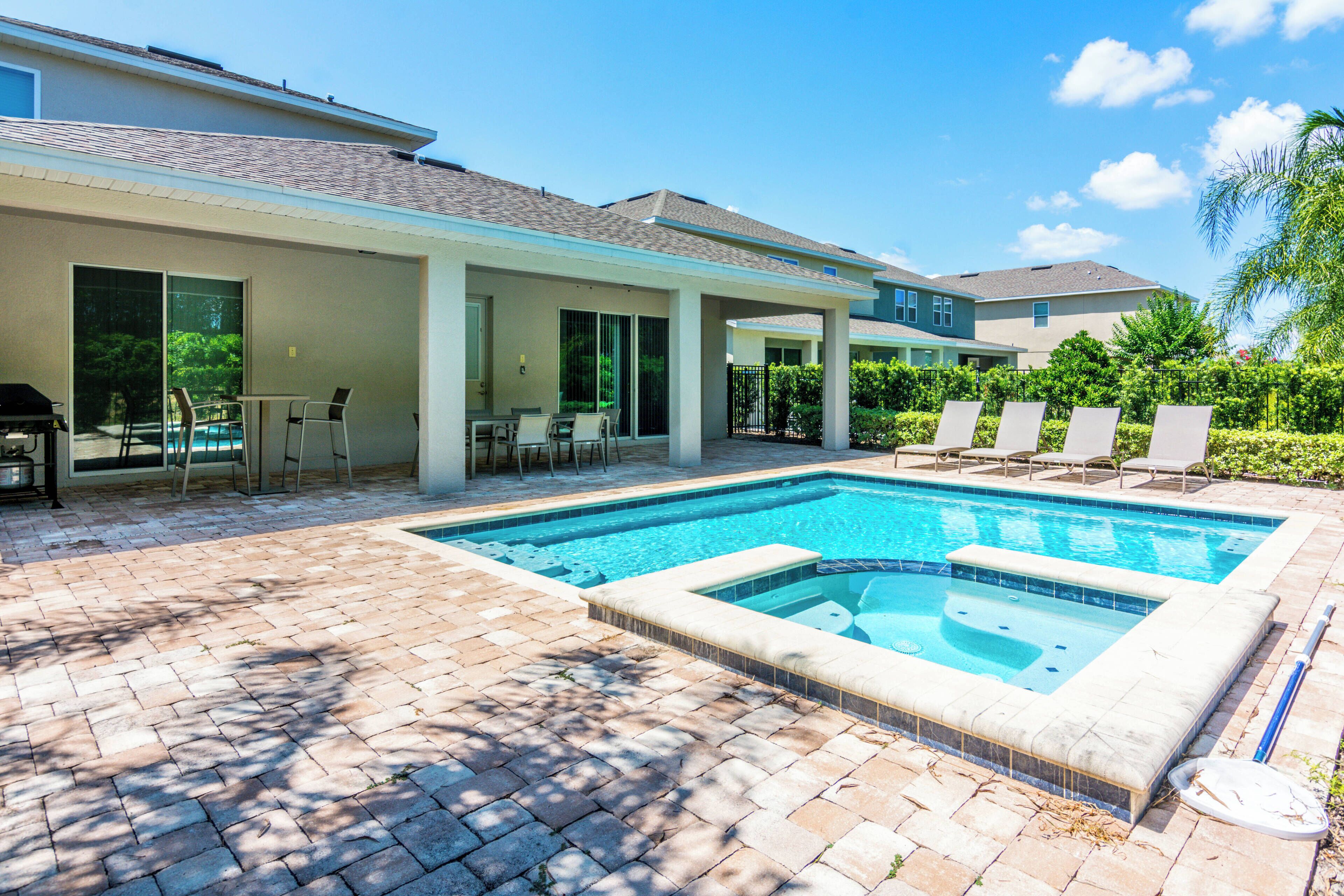 A swimming pool with lounge chairs, a covered patio area, and a barbecue setup.