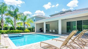 A swimming pool with lounge chairs, a covered patio area, and a view of a residential building. - Gorgeous Single Home With Private Pool at Encore (Kissimmee)
