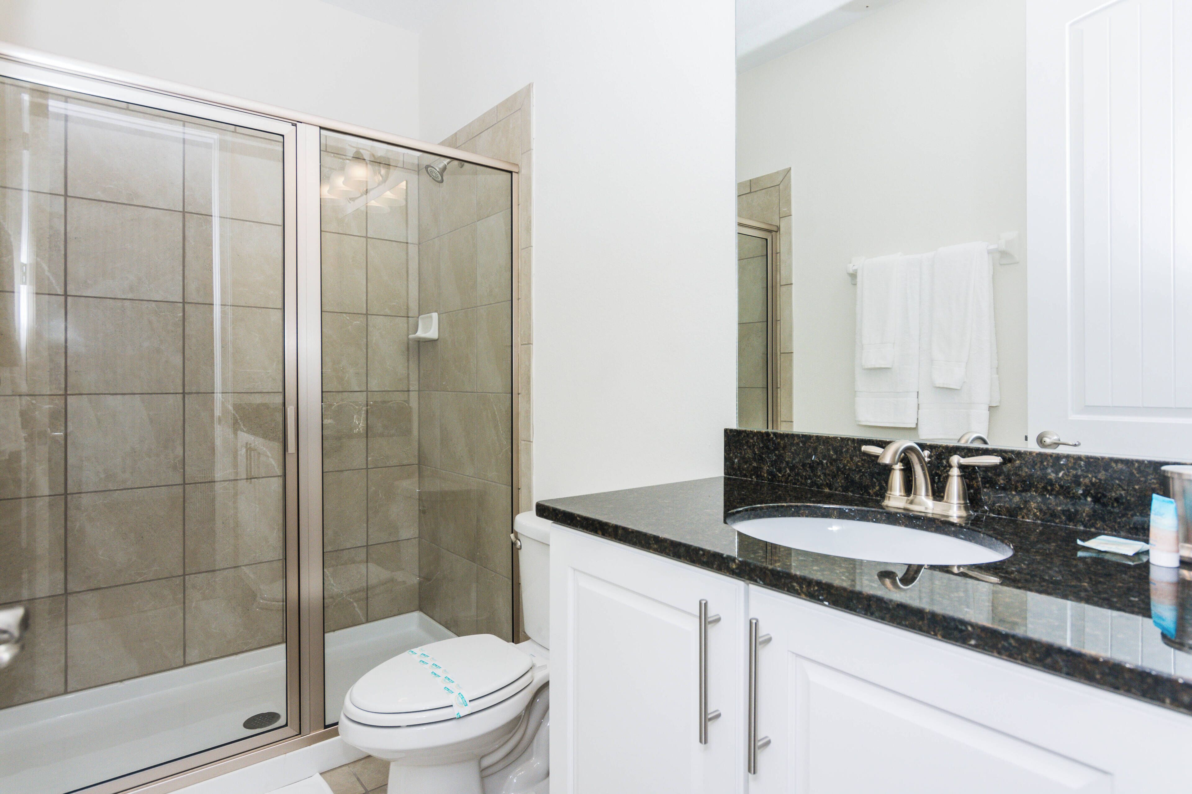 A bathroom with a glass-enclosed shower, a white toilet, a sink with a black countertop, and white cabinets.