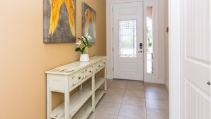 A hallway with a white door, a white console table with drawers, and two paintings of angel wings on the wall. - Gorgeous Single Home With Private Pool at Encore (Kissimmee)