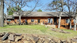 Eine zweistöckige Blockhütte mit Veranda, umgeben von Bäumen und einer Steinschmalseite.