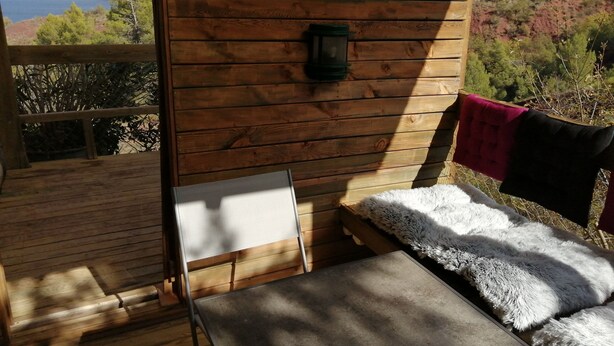 A wooden deck with a bench and a table, overlooking a scenic landscape with trees and a mountain.