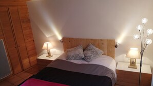 A bedroom with a wooden headboard, two bedside lamps, a bed with a red blanket, and a nightstand with a lamp.