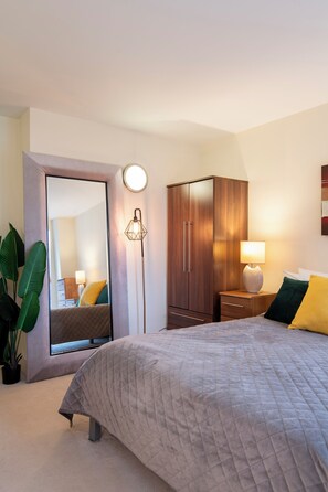 A bedroom with a bed, a wardrobe, a mirror, a floor lamp, and a potted plant.