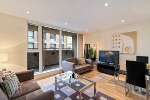 A modern living room with a glass coffee table, a sofa, a TV, and a dining area with chairs.