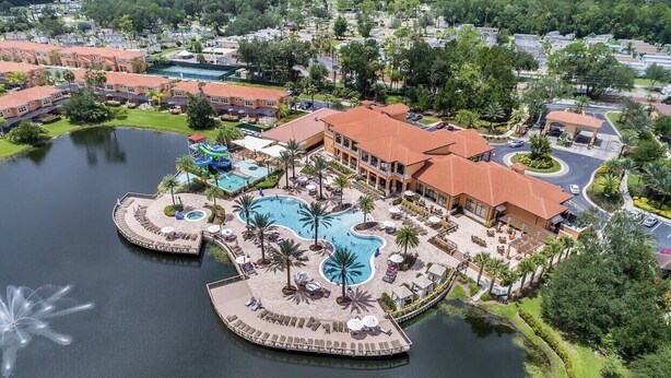 An aerial view of a resort with a large central pool, multiple smaller pools, and a variety of outdoor seating areas surrounded by palm trees. - Comfortable 4br w/ private jacuzzi (Kissimmee)
