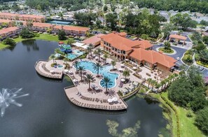 An aerial view of a resort with a large central pool, multiple smaller pools, and a variety of outdoor seating areas surrounded by palm trees. - Comfortable 4br w/ private jacuzzi (Kissimmee)