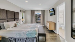 A modern bedroom with a large bed, a bench, a dresser, and a TV on the wall. - Comfortable 4br w/ private jacuzzi (Kissimmee)