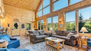 A spacious living room with large windows, wooden walls, and a fireplace. - Big Bear Lodge Retreat where friends & families gather and meet! (Comins)