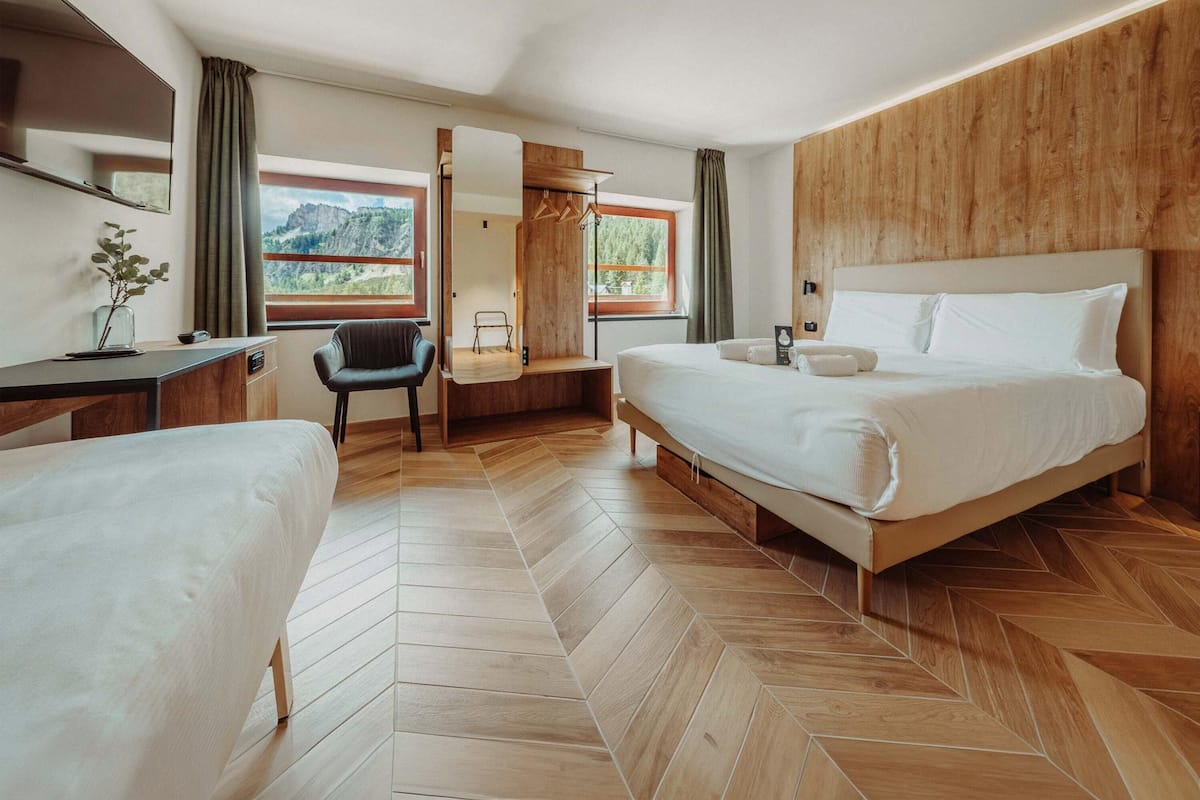 A hotel room with a bed, a desk, a chair, a mirror, and a view of the outdoors.