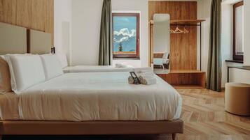 A hotel room with a large bed, a wooden wardrobe, a seating area with a view of mountains, and a small table.