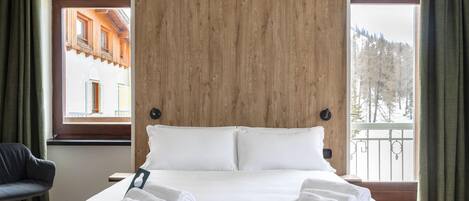 Une chambre d’hôtel avec un grand lit, deux oreillers et une vue sur un immeuble et des arbres, visible par la fenêtre.