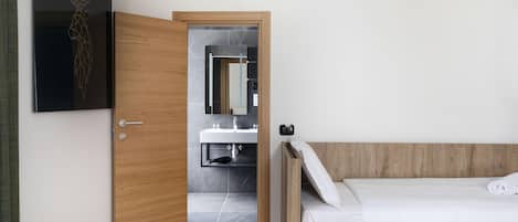 Un dormitorio moderno con puerta de madera que da al baño, una cama con ropa de cama blanca y un espejo montado en la pared.