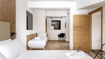 A modern hotel room with a large bed, a smaller bed, a chair, and a wooden door.