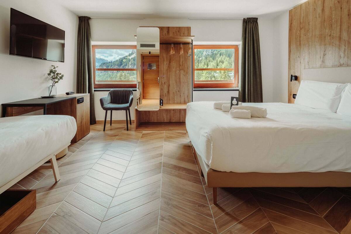 A modern hotel room with a bed, a desk, a chair, and a TV.