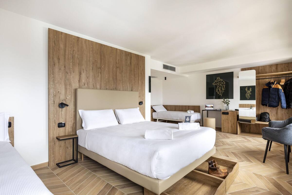 A modern hotel room with a large bed, a desk, a chair, and a wardrobe.