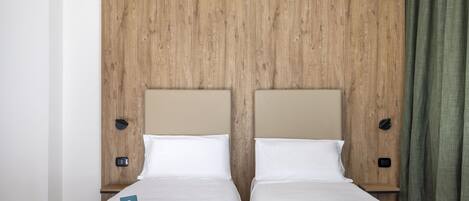 Una cama doble con sábanas blancas, dos mesitas de noche, un cabecero de madera y una cortina verde.