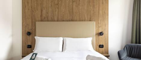 Une chambre d’hôtel avec une tête de lit en bois, du linge de lit blanc, une chaise noire et une paire de serviettes sur le lit.